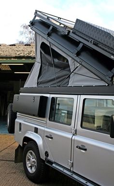 a silver land rover parked in front of a building with its roof open and the door opened