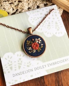 a necklace with a red rose on it sitting on top of a wooden table next to a card