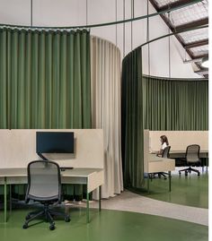 an office with green curtains and white desks in front of a woman sitting at a computer