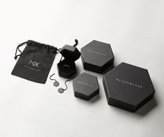 three black jewelry boxes sitting next to each other on a white surface with a drawstring bag