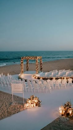 an outdoor ceremony set up on the beach with candles and flowers in front of it