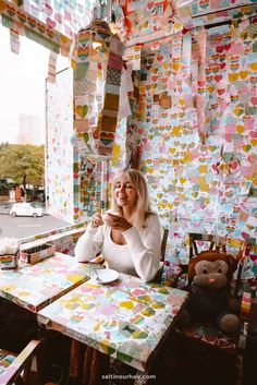 a woman sitting at a table in front of a wall covered with colorful paper hearts