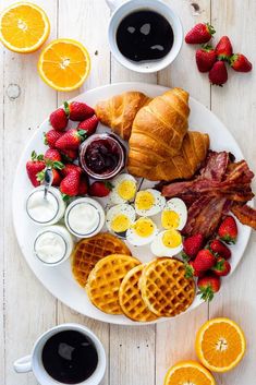 breakfast platter with bacon, eggs, croissants, strawberries and orange juice