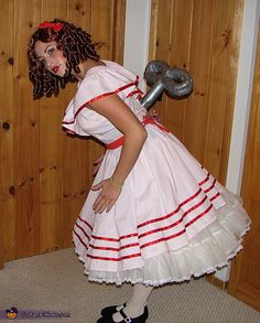 a woman dressed as a girl holding a wrench in her right hand and wearing a white dress with red trim