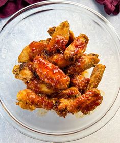 a glass bowl filled with chicken wings covered in ketchup