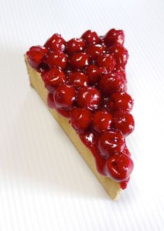 a slice of pie with cherries on top sitting on a white surface, ready to be eaten