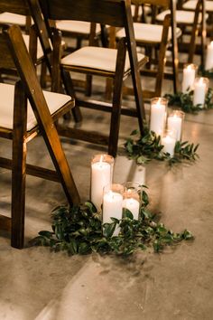 candles are lined up on the floor in front of rows of chairs with greenery