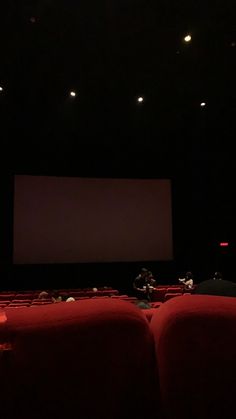 an empty theater with red seats and people sitting on the chairs watching something in front of them