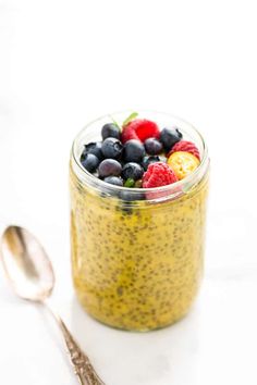 a glass jar filled with fruit on top of a white table next to a spoon