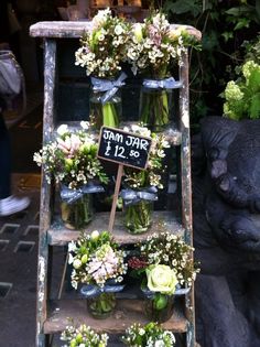 flowers are arranged in vases on an old ladder for sale at a flower shop