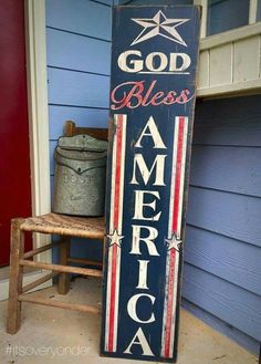 a wooden sign that says god bless america with an american flag on it sitting in front of a blue house