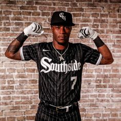 a baseball player is posing for a photo in front of a brick wall with his hands behind his head