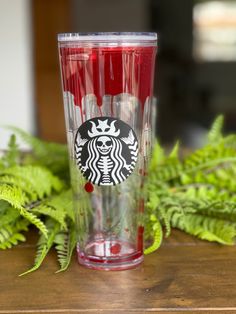 a red starbucks cup sitting on top of a wooden table next to green plants and leaves