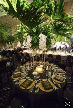 a table set up for an event with place settings and greenery in the center