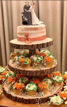 three tiered wedding cake with cupcakes and flowers on the bottom, decorated with an orange ribbon