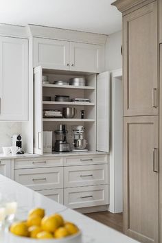 a bowl of lemons sits on the counter in this white kitchen with gray cabinets