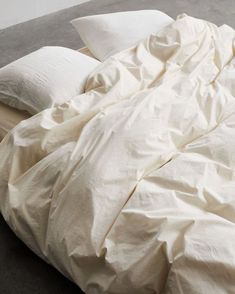 an unmade bed with white sheets and pillows on top of it, next to a wall