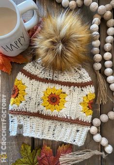 a knitted hat with sunflowers on it next to a cup of coffee