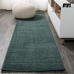 a green rug in a living room next to a white dresser and window with curtains