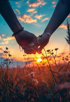 two people holding hands in the middle of a grassy field with the sun setting behind them