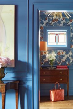 a room with blue walls and floral wallpaper, an orange purse on the floor