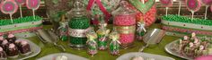 a table topped with lots of desserts and candies covered in pink and green frosting