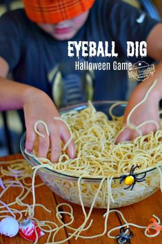 a young boy is playing with noodles in a bowl and spider webs are on the table