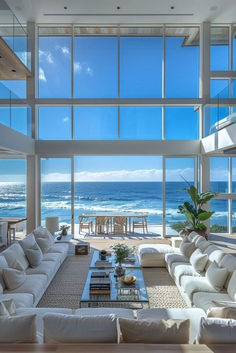 a living room filled with white furniture and large windows overlooking the ocean on a sunny day