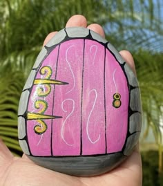 a hand is holding a painted rock with the word sas written on it and palm trees in the background