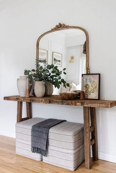 a wooden table sitting next to a mirror on top of a white wall with potted plants