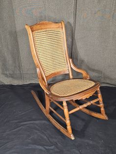 a wooden rocking chair with wicker seat and back rests against a gray background backdrop