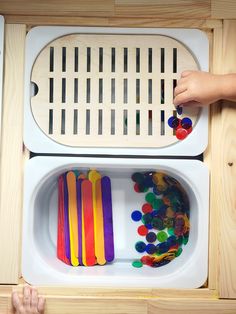 a child's hand reaching into a drawer filled with colorful plastic beads and wooden spoons