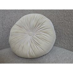 a white round pillow sitting on top of a grey couch next to a gray wall