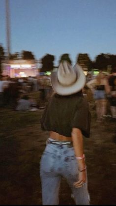 a woman in jeans and a cowboy hat is looking up at the sky while people are standing around