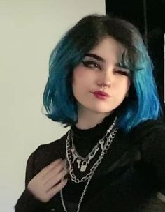 a woman with blue hair wearing a black shirt and silver chains on her necklaces