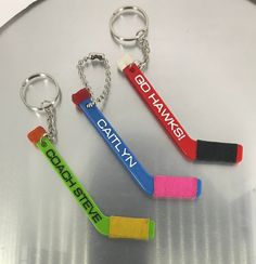 three key chains with different colored crayons attached to them on a silver surface