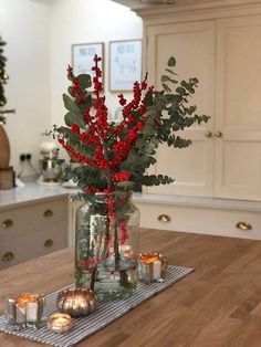 a vase filled with flowers and candles on top of a wooden table in a kitchen