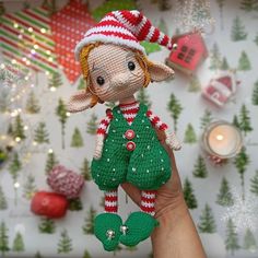 a hand holding up a small doll made out of knitted material with christmas decorations in the background