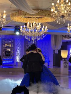 two people hugging each other in the middle of a dance floor with chandeliers