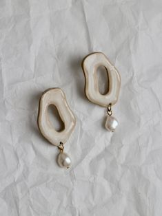 two white earrings with pearls hanging from them on top of a piece of parchment paper