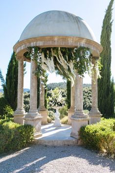 an outdoor gazebo with white flowers and greenery on the top, surrounded by trees