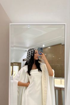 a woman taking a selfie in front of a mirror wearing a white dress and shawl