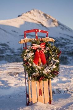 a wooden sled decorated with wreaths and bows in the snow next to a mountain