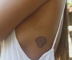 a woman with a shell tattoo on her upper arm and shoulder, behind her is a white tank top