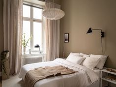 a white bed sitting under a window next to a lamp