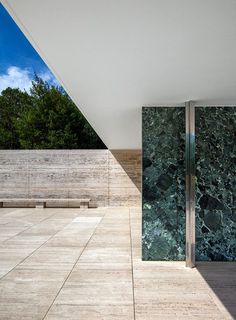 an outdoor area with wooden benches and green marble wall covering the entire space, along with glass doors