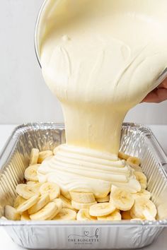 a person pouring cream over sliced bananas in a tin pan on top of a counter