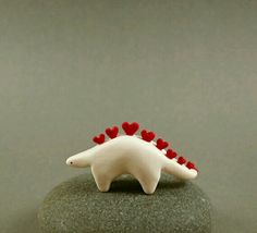 a small white dinosaur with red hearts on its back sitting on top of a rock