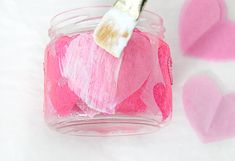 a small jar filled with pink hearts and a paint brush on top of the jar