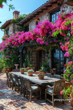 an outdoor dining table surrounded by potted plants and flowers on the side of a house